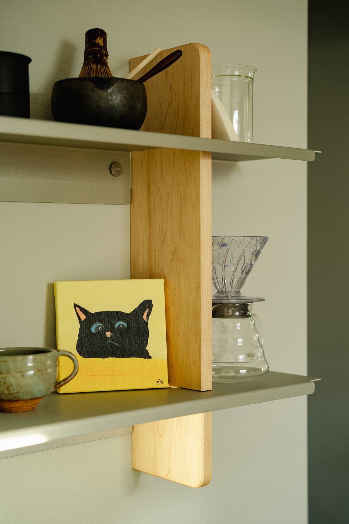 A clear pour-over brewer and coffee server on a shelf beside ceramics and artwork