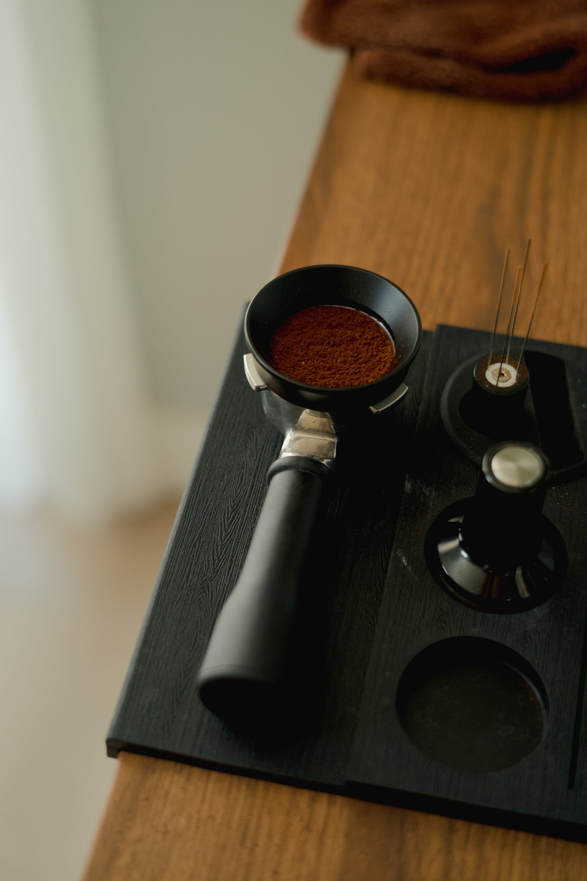 Portafilter with grounds and espresso prep tools on a black tamping mat